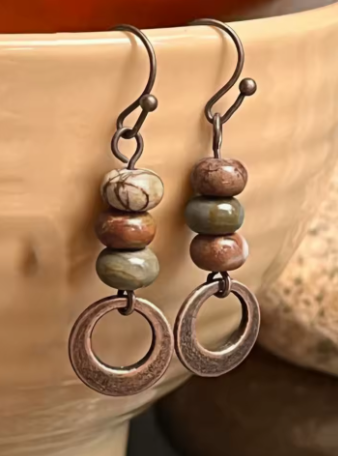 Pair of earrings with brown and green beads and circular metal elements on a beige background.