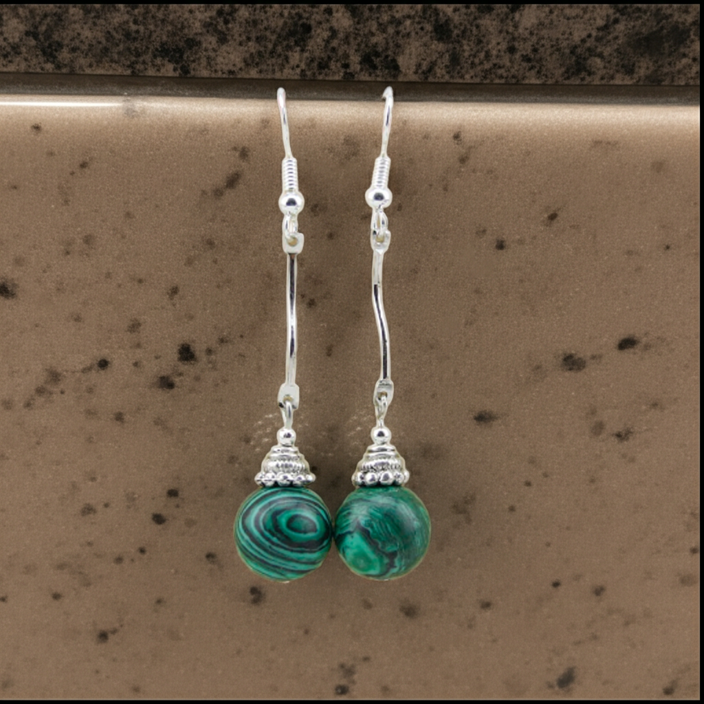 Silver earrings with green beads on a brown surface