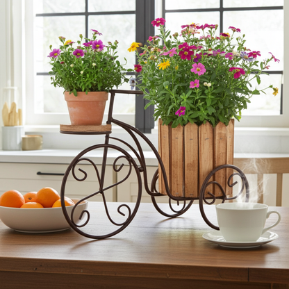 Decorative bicycle planter with flowers on a table next to a bowl of oranges and a cup.
