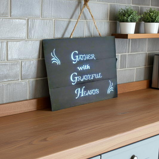 Decorative sign with text 'Gather with Grateful Hearts' on a wooden surface.