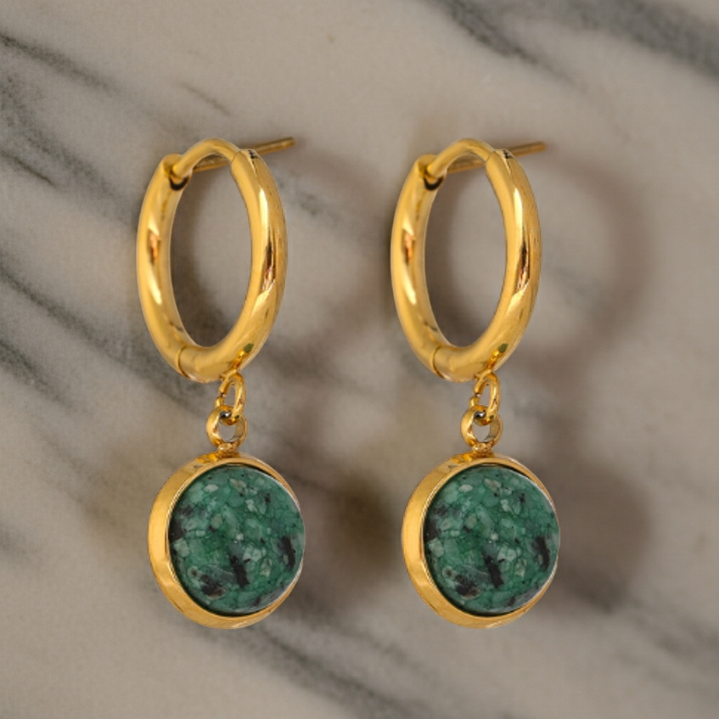 Gold hoop earrings with green stone drops on a marble background
