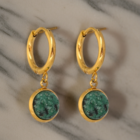 Gold hoop earrings with green stone drops on a marble background