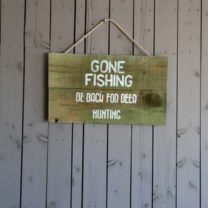 Wooden sign with text 'Gone Fishing, Be Back For Deer Hunting' on a wooden background