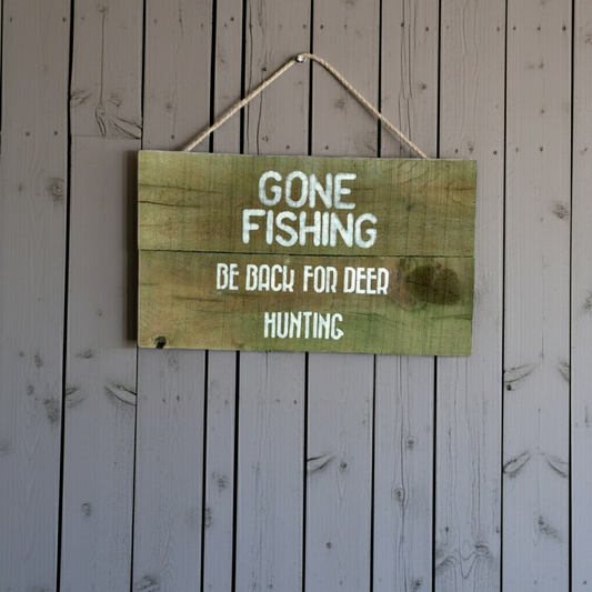 Wooden sign with text 'Gone Fishing, Be Back For Deer Hunting' on a wooden background