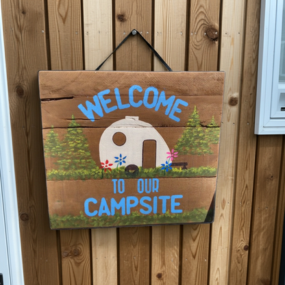 Wooden sign with 'Welcome to our Campsite' text and camper illustration on a wooden background