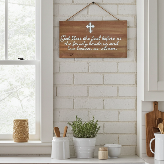 Wooden sign with a prayer on a kitchen wall with a window and plants.