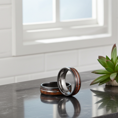 Two wooden and metal rings on a reflective surface with a plant in the background.