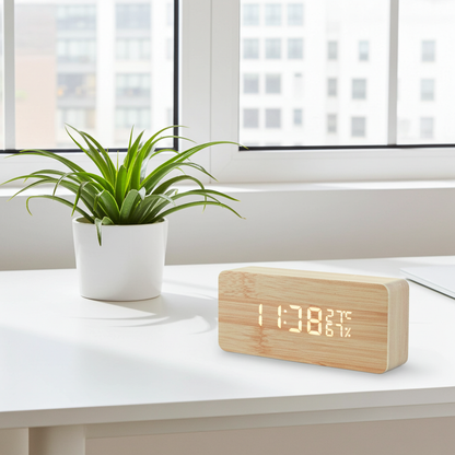 Wooden digital clock displaying time and temperature on a white surface with a plant in the background.