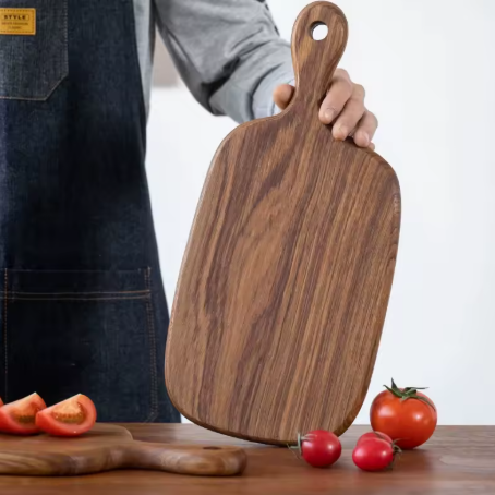 Person holding a wooden cutting board with tomatoes on a table