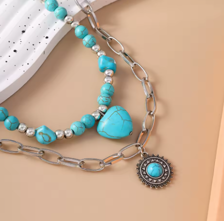 Turquoise beaded bracelet with silver chain and decorative charm on a beige background