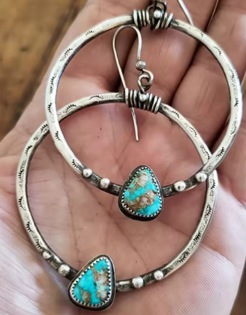 Silver hoop earrings with turquoise heart stones held in a hand.