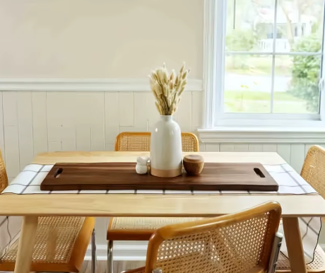 Dining room with a table set for a meal, featuring a vase with flowers and a cutting board.