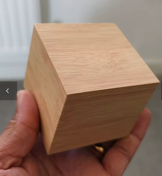 Wooden cube held in a hand with a neutral background