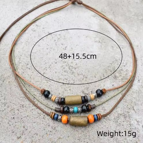 A multi-strand cord necklace with decorative beads and two central metallic cylindrical charms, shown on a light gray textured surface. Black oval line art and text indicate a size of 48+15.
