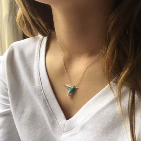 Person wearing a necklace with a green pendant on a plain background