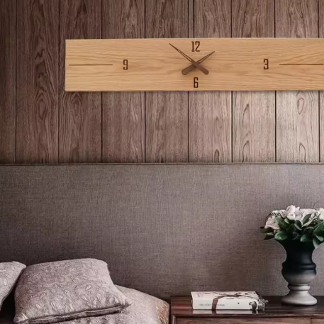 Wooden wall clock on a wooden wall with a vase and books on a table below.