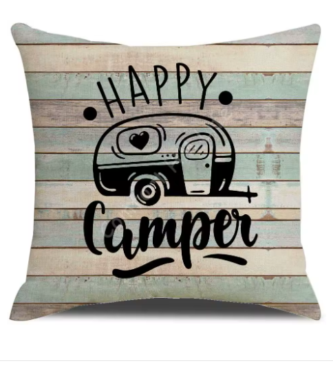 Pillow with 'Happy Camper' text and camper illustration on a wooden planks background