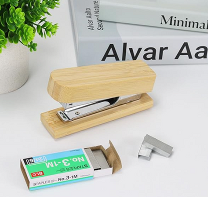Wooden stapler with staples on a white surface, with 'Alvar Aalto' branding in the background.
