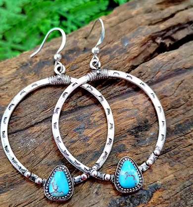 Silver hoop earrings with turquoise stones on a wooden surface