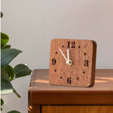 Wooden clock on a wooden surface with a plant in the background