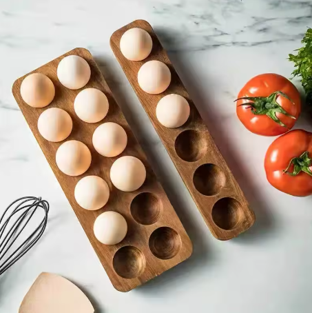 Wooden egg trays with eggs on a marble surface with tomatoes and a whisk.
