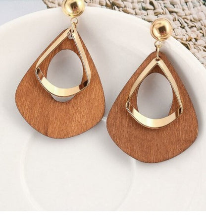 A pair of wooden triangle-shaped earrings with gold trim, displayed on a table with a white plate and coconut mat in the background.